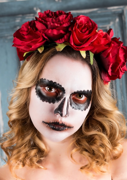 El retrato de una mujer joven con Halloween compone con las flores rojas.