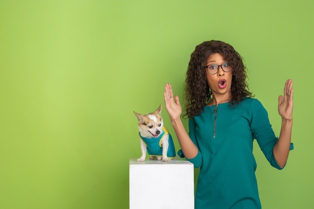 Retrato de mujer joven hermosa afroamericana con perrito sobre fondo verde de estudio