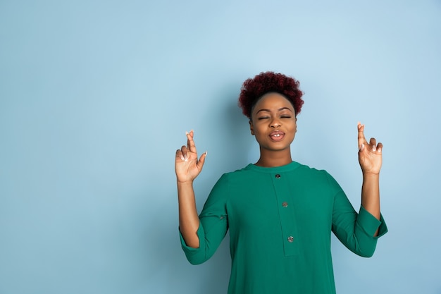 Retrato de mujer joven hermosa afroamericana sobre fondo azul de estudio, expresivo emocional.