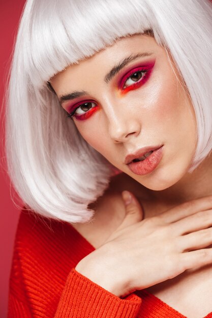 Retrato de mujer joven hermosa aislada en la pared roja con maquillaje brillante posando.