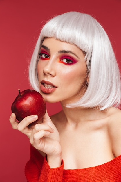 Retrato de mujer joven hermosa asombrosa aislada en la pared roja que sostiene la manzana.