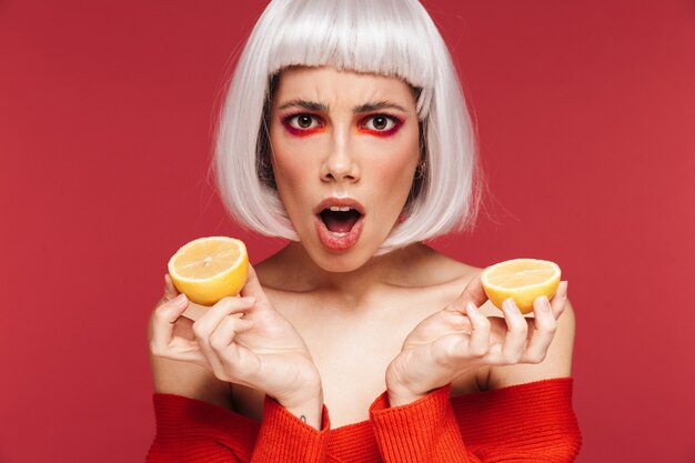 Retrato de mujer joven hermosa emocional disgustada aislada en la pared roja con limón.