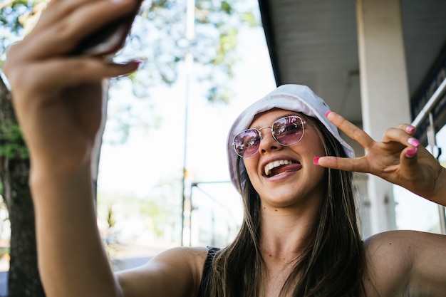 Retrato de una mujer joven, hermosa y feliz tomando una foto de sí misma y mostrando el signo de la victoria