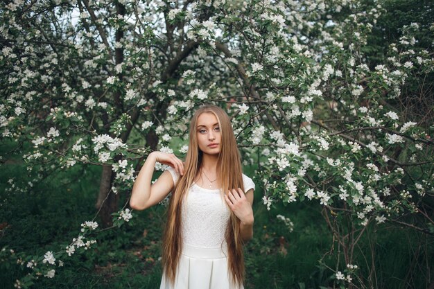 Retrato de mujer joven hermosa en la floración de los manzanos. Elegante chica en vestido blanco con flores de manzano