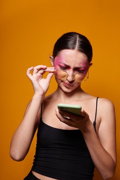 Retrato de mujer joven hermosa con gafas maquillaje brillante posando jersey negro hablando por teléfono primer plano inalterado