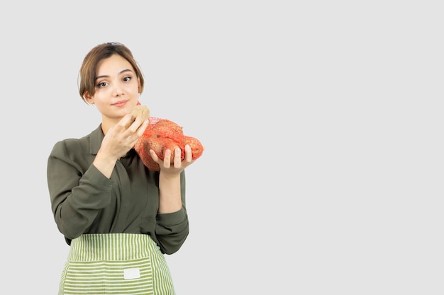 Retrato de una mujer joven hermosa del granjero que sostiene las patatas en la bolsa. Foto de alta calidad