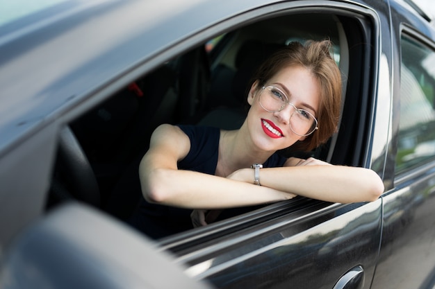 Un retrato de mujer joven hermosa oficina con maquillaje brillante, labios rojos se sienta en un auto negro