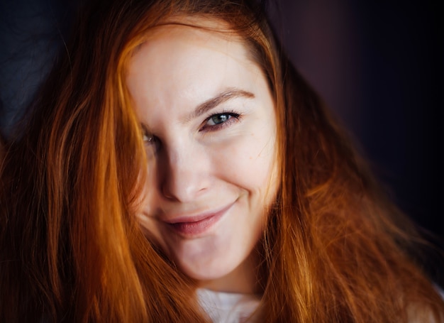 Retrato de mujer joven hermosa con pelo rojo espeso y despeinado, primer plano. Belleza de ojos grises mirando a cámara y sonriendo. Publicidad de productos para el cuidado de la piel o el cabello.