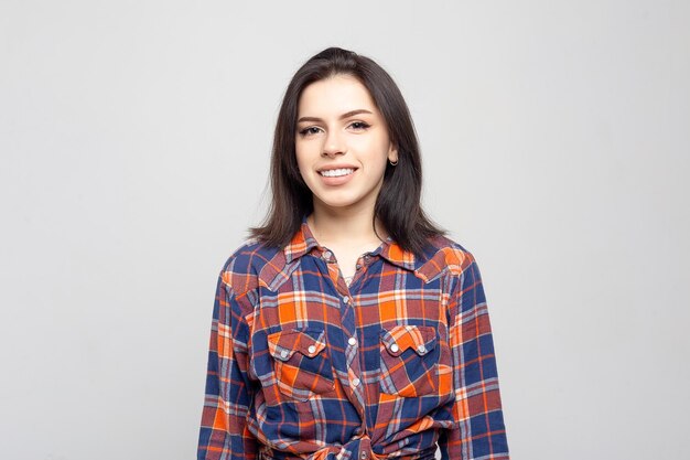 Retrato de mujer joven hermosa Retrato de una hermosa morena sonriente en una camisa a cuadros en un blanco gris