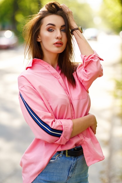 Retrato de mujer joven y hermosa en ropa casual en la calle. vestida con una camisa rosa y jeans. concepto de primavera / verano. tiempo de relajación. Chica de ojos azules. Disfruta de la puesta de sol en la calle