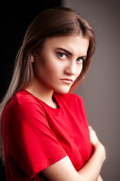 Retrato mujer joven hermosa seria en camiseta roja y jeans posando con las manos en la cadera