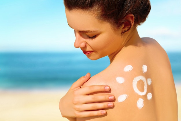 Retrato de mujer joven hermosa sonriendo en bikini con el sol dibujado en un hombro en la playa