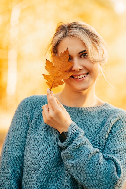 Retrato de mujer joven hermosa en suéter de punto de color azul escondido detrás del follaje de otoño