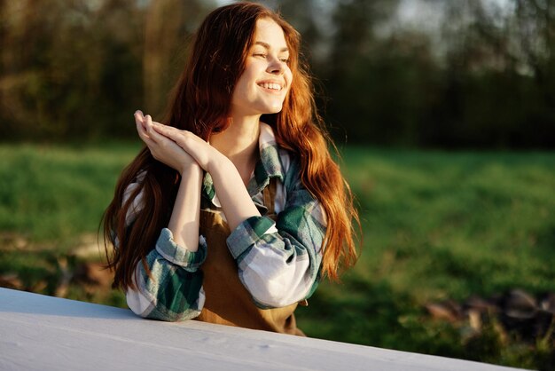 Retrato de una mujer joven con un hermoso cabello largo y rojo con una hermosa sonrisa con dientes contra un parque verde bajo la luz del sol del atardecer de verano