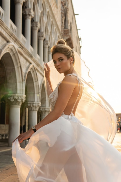 Retrato de mujer joven con hermoso vestido blanco caminando por una calle de la ciudad de Venecia