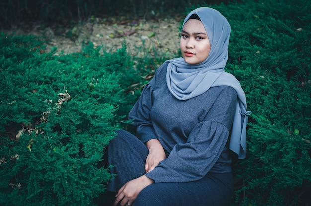 Retrato de una mujer joven en hijab sentada en medio de plantas en el campo