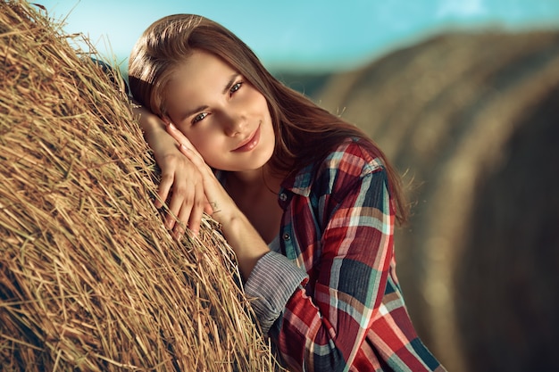 Retrato de mujer joven junto a una pila de heno en la luz del sol