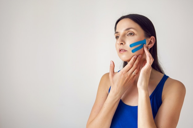 Retrato de una mujer joven con konesiotape pegado para rejuvenecimiento y estiramiento facial sin cirugía