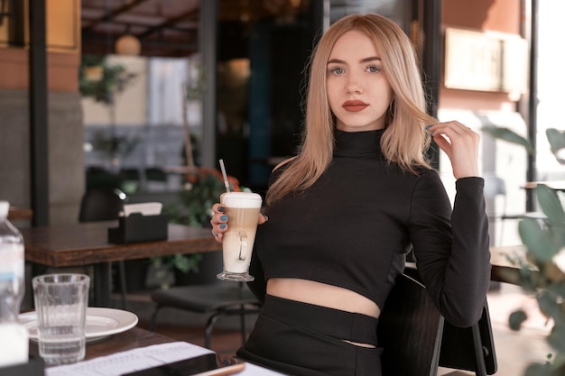 Retrato de mujer joven con labios rojos viste ropa negra y sostiene una taza de capuchino