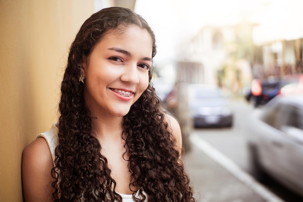 Retrato de mujer joven latinoamericana sonriendo con corchetes sobre la ciudad de la calle