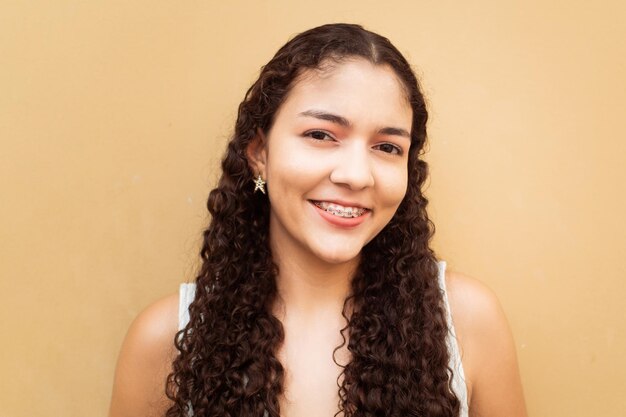 Retrato de mujer joven latinoamericana sonriendo con corchetes sobre el color de la pared amarillo