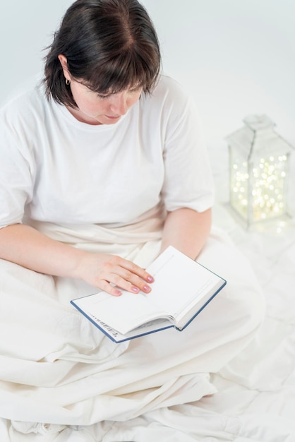 Retrato de mujer joven con libro en manos. Leer antes de acostarse. Ambiente acogedor, tiempo para ti.