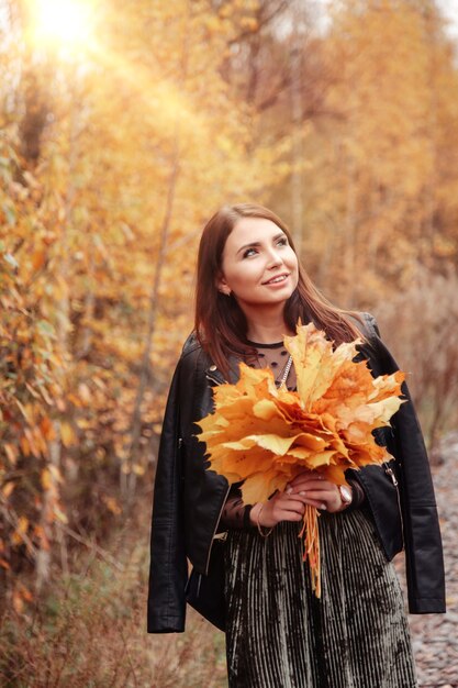 Retrato de mujer joven linda de apariencia eslava con hojas en ropa casual en otoño, contra el fondo de un parque de otoño. Bonita mujer caminando en el parque en otoño dorado. Copia espacio