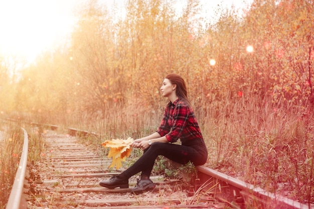 Retrato de mujer joven linda de apariencia eslava en ropa casual en otoño, en la vía férrea con el telón de fondo de un parque y un río de otoño. Bonita mujer caminando en el bosque en otoño dorado. Copia espacio