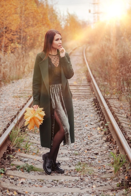 Retrato de mujer joven linda de apariencia eslava en ropa casual en otoño, en la vía férrea con el telón de fondo de un parque y un río de otoño. Bonita mujer caminando en el bosque en otoño dorado. Copia espacio