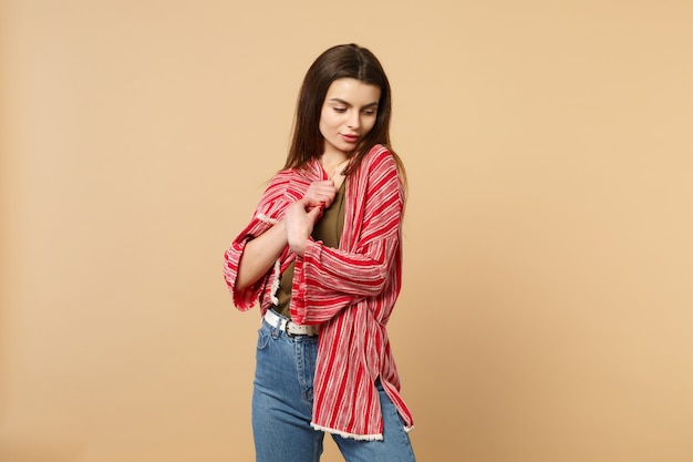 Retrato de mujer joven linda atractiva en ropa casual de pie, mirando hacia abajo aislado sobre fondo de pared beige pastel en estudio. Personas sinceras emociones, concepto de estilo de vida. Simulacros de espacio de copia.