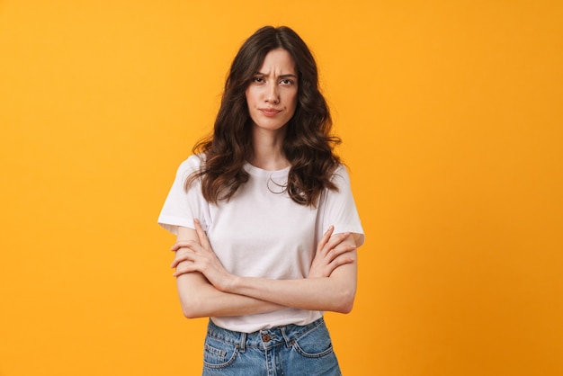 Retrato de mujer joven linda enojada disgustada posando aislada sobre pared amarilla con los brazos cruzados