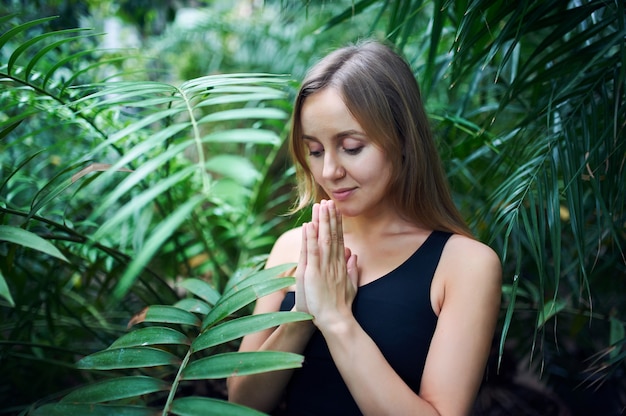 Retrato de mujer joven linda meditando y haciendo namaste mano en la selva.