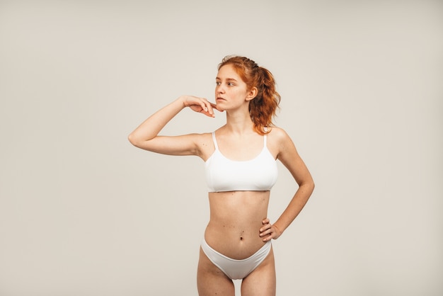 Retrato de mujer joven linda pelirroja con pelo largo ondulado y pecas viste ropa interior blanca