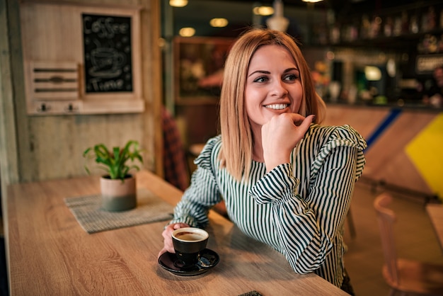 Retrato de una mujer joven linda que se sienta en el café de consumición de la barra.