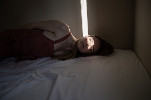 Retrato de mujer joven con una línea de luz iluminando sus ojos acostada en la cama