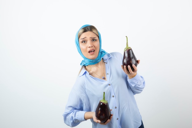 Retrato de mujer joven en mantón azul sosteniendo berenjenas crudas