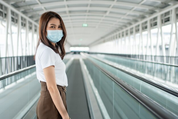 Retrato de una mujer joven con una máscara médica en la cinta mecánica del aeropuerto