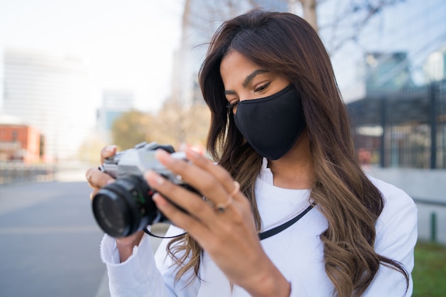 Retrato de mujer joven con máscara protectora y con cámara mientras toma fotografías en la ciudad. Nuevo concepto de estilo de vida normal.