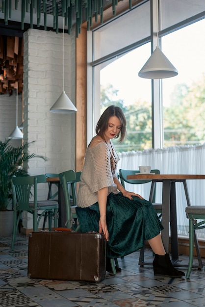 Retrato de mujer joven en la mesa de café con maleta retro Mujer turista emigrante extranjera en café