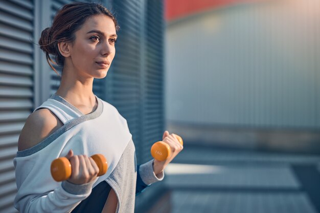 Retrato de una mujer joven con una mirada de ensueño sosteniendo las pesas en sus manos