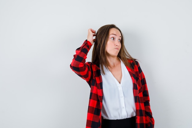 Retrato de mujer joven mirando a un lado, rascándose la cabeza con ropa casual y mirando pensativo vista frontal