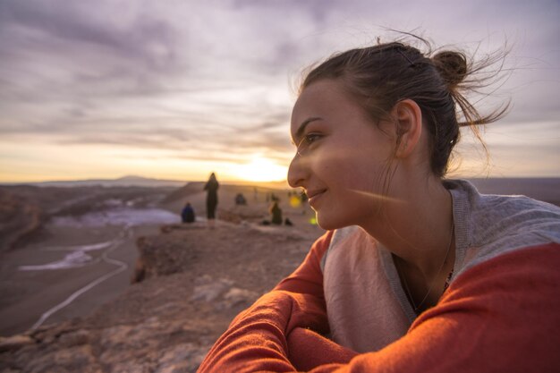 Foto retrato de una mujer joven mirando a la playa contra el cielo durante la puesta de sol