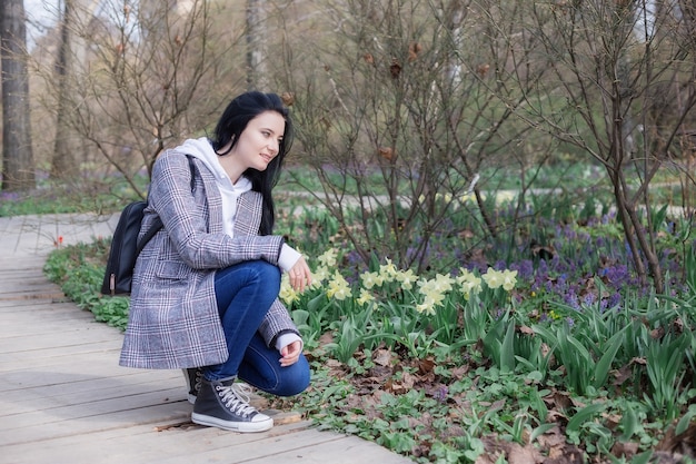 Retrato de mujer joven morena con un abrigo a cuadros en el parque y mirando a otro lado disfrutando de la naturaleza en el hermoso día de primavera