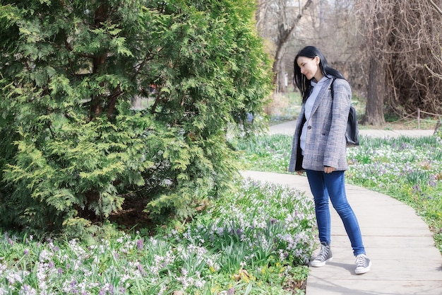 Retrato de mujer joven morena con un abrigo a cuadros en el parque y mirando a otro lado disfrutando de la naturaleza en el hermoso día de primavera