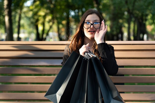 Retrato de mujer joven morena con bolsas de la compra en un banco en el parque.