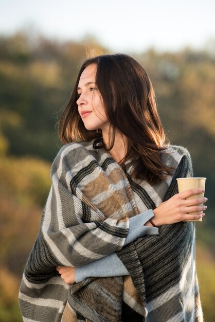 Retrato de mujer joven morena en una cálida manta y una taza de café en sus manos. Belleza natural. Marco vertical.