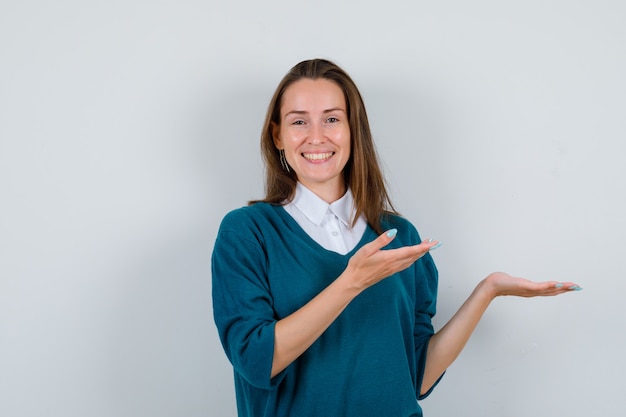 Retrato de mujer joven mostrando o presentando algo en la pared blanca con espacio de copia