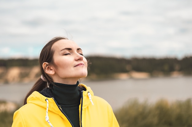 Foto retrato de una mujer joven en la naturaleza en una chaqueta amarilla respirando aire fresco limpio y fresco de otoño