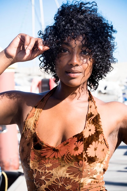 Retrato de mujer joven negra atractiva con vestido de verano mirando a la cámara Hermosa chica de cabello étnico disfruta del sol y el estilo de vida de día al aire libre posando como modelo