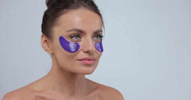 Retrato de mujer joven con parches violetas en la cara fondo gris del estudio Concepto de productos de belleza y cuidado de la piel